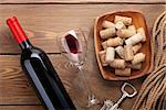 Red wine bottle, glass of wine, bowl with corks and corkscrew. View from above over rustic wooden table background