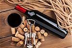 Red wine bottle, glass, corks and corkscrew. View from above over rustic wooden table background