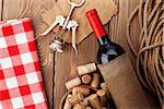 Red wine bottle, bowl with corks and corkscrew. View from above over rustic wooden table background