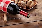 Red wine bottle, bowl with corks and corkscrew. Closeup over rustic wooden table background