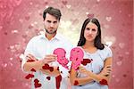 Upset couple holding two halves of broken heart against valentines heart design