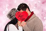 Young couple kissing behind red heart against valentines heart design