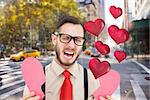 Geeky hipster crying and holding broken heart card against blurry new york street