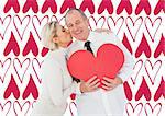 Older affectionate couple holding red heart shape against valentines day pattern