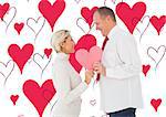 Older affectionate couple holding pink heart shape against valentines day pattern