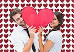 Couple smiling at camera holding a heart against valentines day pattern