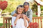 Elderly man hugging his wife who is on the bench against hearts