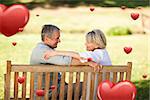 Happy retired couple sitting on the bench against hearts