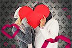 Couple in winter fashion posing with heart shape against grey wallpaper