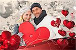 Smiling couple in winter fashion posing with heart shape against grey valentines heart pattern