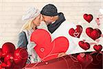 Smiling couple in winter fashion posing with heart shape against white wall