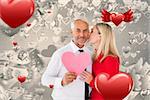 Handsome man holding paper heart getting a kiss from wife against grey valentines heart pattern