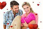 Attractive young couple sitting holding heart cushion against hearts