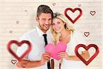 Attractive young couple holding pink heart against white wall