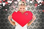 Attractive young blonde showing red heart against grey wallpaper