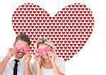 Attractive young couple holding pink hearts over eyes against valentines day pattern