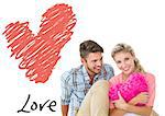Attractive young couple sitting holding heart cushion against love heart