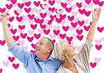 Happy mature couple with hands up against valentines day pattern