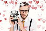 Geeky hipster holding a retro camera against valentines heart design