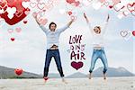 Cheerful young couple jumping at beach against love is in the air