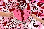 Hands holding two halves of broken heart against digitally generated girly heart design
