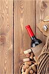 Red wine bottle, corks and corkscrew on wooden table background with copy space