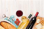 White and red wine glasses, cheese and bread on white wooden table background with copy space