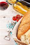 White and red wine glasses, tomatoes and bread on white wooden table background