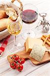 White and red wine glasses, cheese and bread on white wooden table background