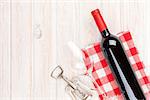 Red wine bottle, glass and corkscrew on white wooden table background with copy space
