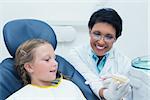 Female dentist teaching girl how to brush teeth in the dentists chair
