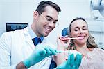 Male dentist teaching woman how to brush teeth in the dentists chair