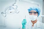 Portrait of female dentist in surgical mask and safety glasses holding hook