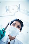 Low angle view of female dentist in surgical mask holding dental drill
