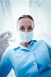 Low angle portrait of female dentist in surgical mask holding injection