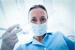 Low angle portrait of female dentist in surgical mask holding injection