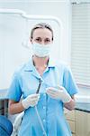 Portrait of female dentist in surgical mask holding dental tool
