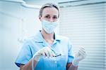 Portrait of female dentist in surgical mask holding dental tools