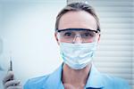 Portrait of female dentist in surgical mask and safety glasses holding injection