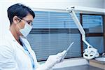 Concentrated female dentist in surgical mask using digital tablet