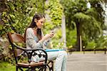 Smiling student sitting on bench text message on her mobile phone in park at school