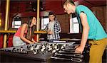 Smiling friends student playing table football in competition in a pub