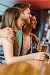 Smiling brown hair standing with arm around his friends in a bar