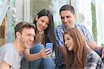 Happy students looking at smartphone outside on campus at the university