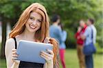 Pretty student smiling at camera using tablet pc at the university