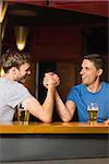 Happy friend arm wrestling each other in a bar