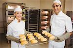 Team of bakers holding rack of rolls in a commercial kitchen