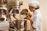 Baker pouring flour into large mixer in a commercial kitchen