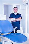 Dentist in blue scrubs smiling at camera beside chair at the dental clinic