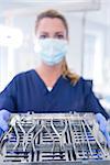 Dentist in blue scrubs holding tray of tools at the dental clinic